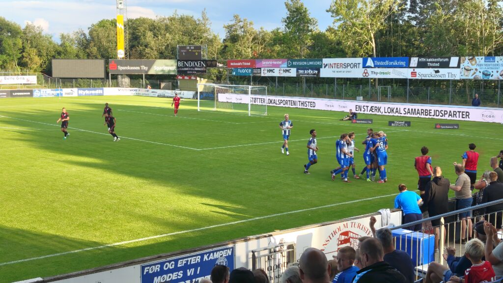 Fußballspiel in der Sparekassen Thy Arena, Thisted FC feiert ein Tor mit jubelnden Spielern und Zuschauern in einem Stadion mit Rasenfeld und Werbebannern.